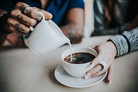 Eine Hand gießt Milch in eine Tasse Kaffee, die von einer anderen Person gehalten wird