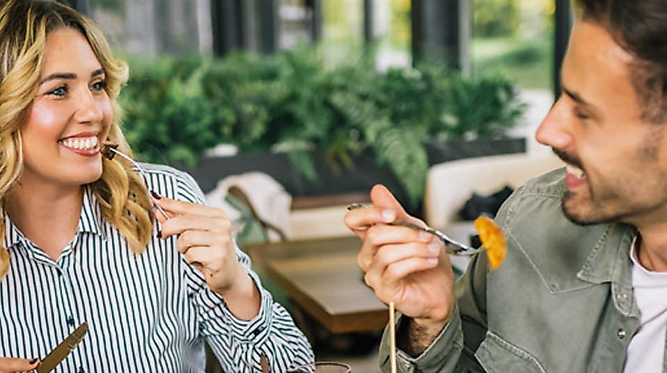 Zwei Männer und eine Frau essen an einem gedeckten Tisch und lachen