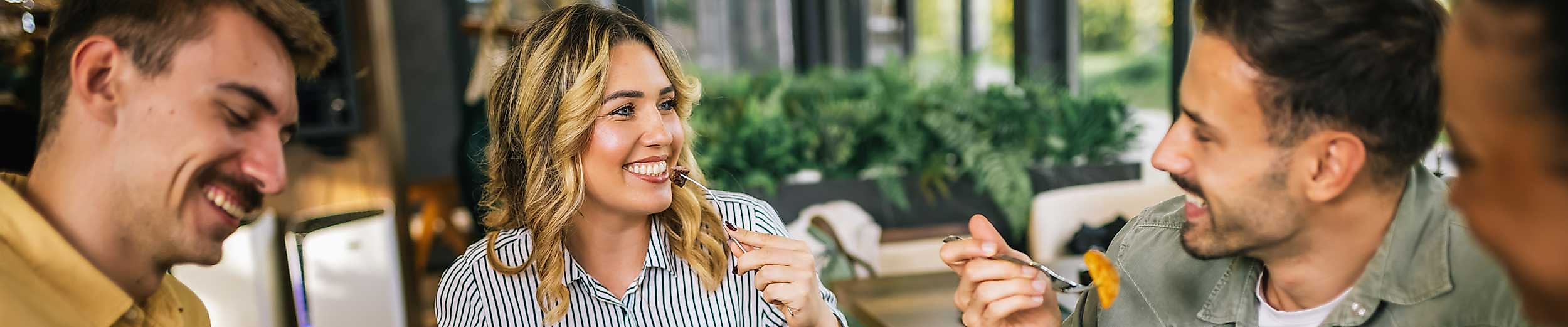 Zwei Männer und eine Frau essen an einem gedeckten Tisch und lachen