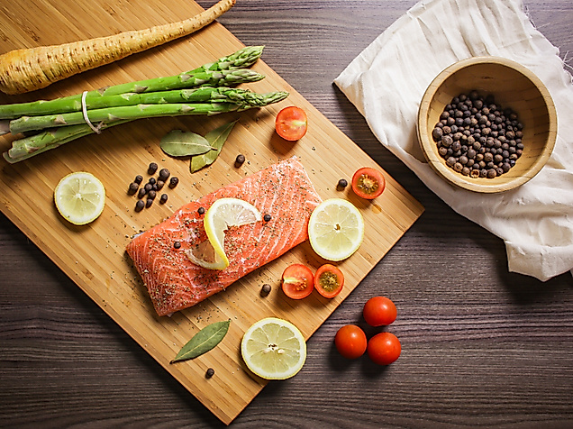 Rohes Lachsfilet mit Zitrone, Gewürzen und Gemüse dekorativ auf Holzbrett angerichtet