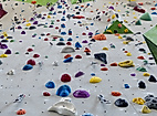 Hohe Indoor-Kletterwand mit bunten Griffen und Sicherungsseilen für verschiedene Schwierigkeitsgrade