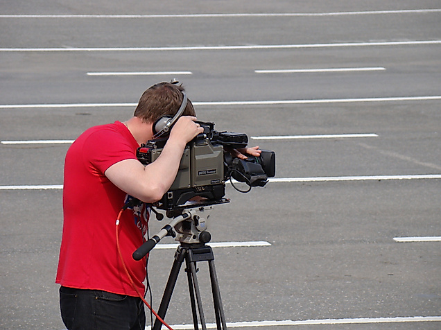 Kameramann mit rotem T-Shirt filmt mit Profi-Equipment auf leerem Asphaltplatz