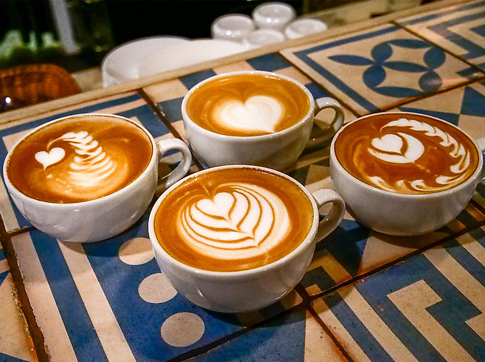 Vier Cappuccinos mit Latte Art auf kunstvoll gemusterter Theke im Kaffeemuseum Hamburg.