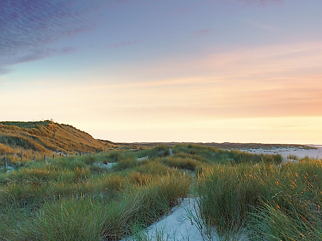 Panoramablick auf Sylt mit Leuchtturm in den Dünen und Sonnenuntergang über der Nordsee