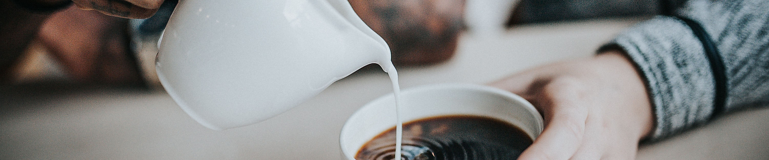 Eine Hand gießt Milch in eine Tasse Kaffee, die von einer anderen Person gehalten wird