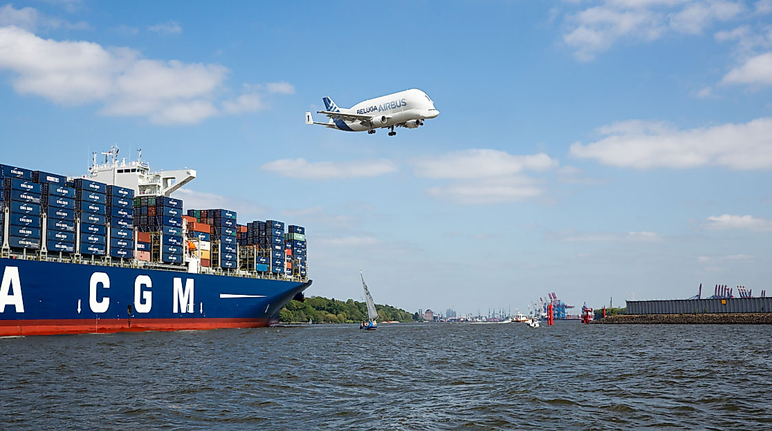 Containerschiff auf der Elbe mit fliegendem Beluga-Frachtflugzeug am Himmel über dem Hamburger Hafen