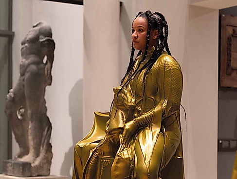 A person wearing a shiny gold-colored suit is on display as an exhibit in the museum.