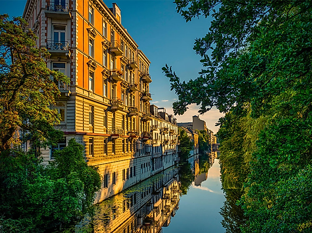 Jugendstilfassaden am Alsterkanal in Hamburg bei Sonnenuntergang, gesäumt von Bäumen und Wasserreflexionen