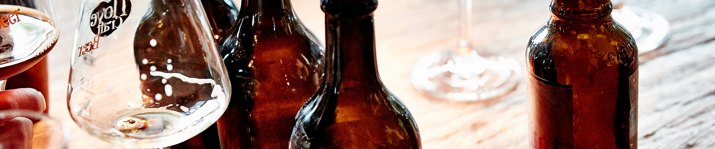 Mehrere Bockbierflaschen und Verkostungsgläser auf Holztisch bei Bier-Event arrangiert